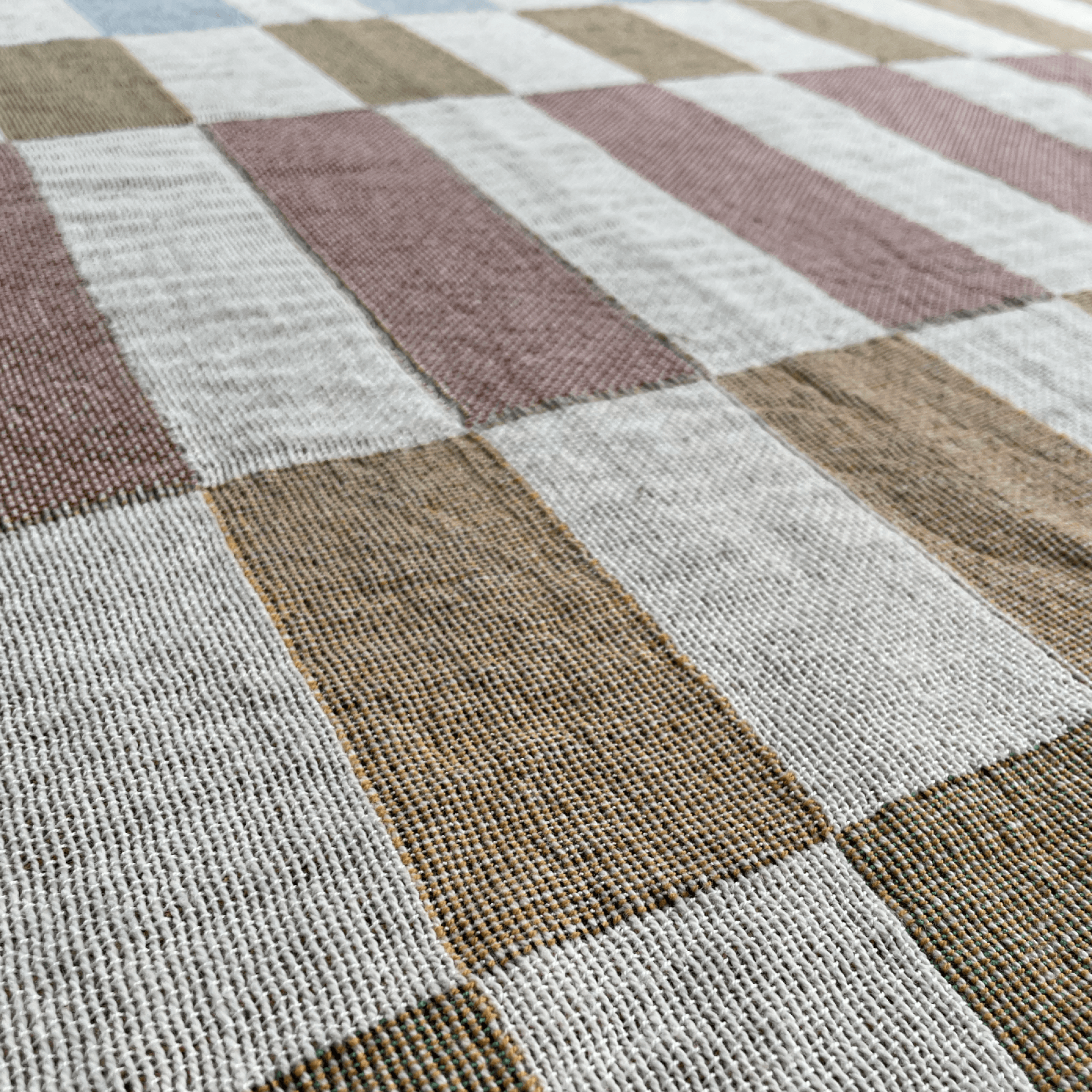A close-up of a woven textile with a large checkered pattern in muted dusty pink, tan, brown, and off-white.
