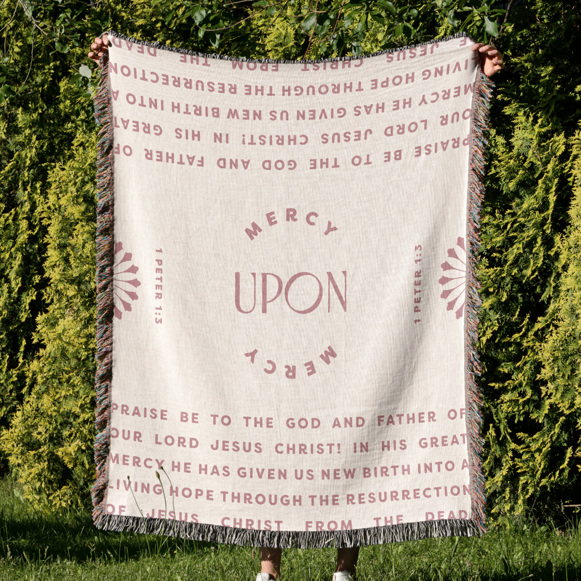 Person holding a blanket with religious text against a green outdoor background