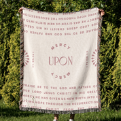 Person holding a blanket with religious text against a green outdoor background