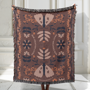Decorative blanket with floral and butterfly pattern held by a person against a white wall.