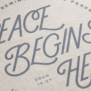Text on fabric with 'Peace Begins Here' and 'John 14:27' printed in gray.