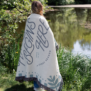 Person wrapped in a blanket with text by a pond