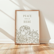 Framed artwork with floral design and 'Peace Dwells Here' text on a wall.