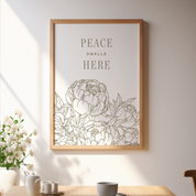 Framed artwork with floral design and 'Peace Dwell Here' text on a wall above a table.