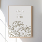 Framed artwork with floral design and 'Peace Dwells Here' text on a white wall.