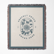 Blanket with floral design and 'Perfect Peace Grows Here' text on a beige background