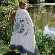 Person wrapped in a blanket with 'Grows Here' text and floral design, standing by a pond.