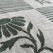 Close-up of a woven textile with a dark green floral motif on a light beige background.