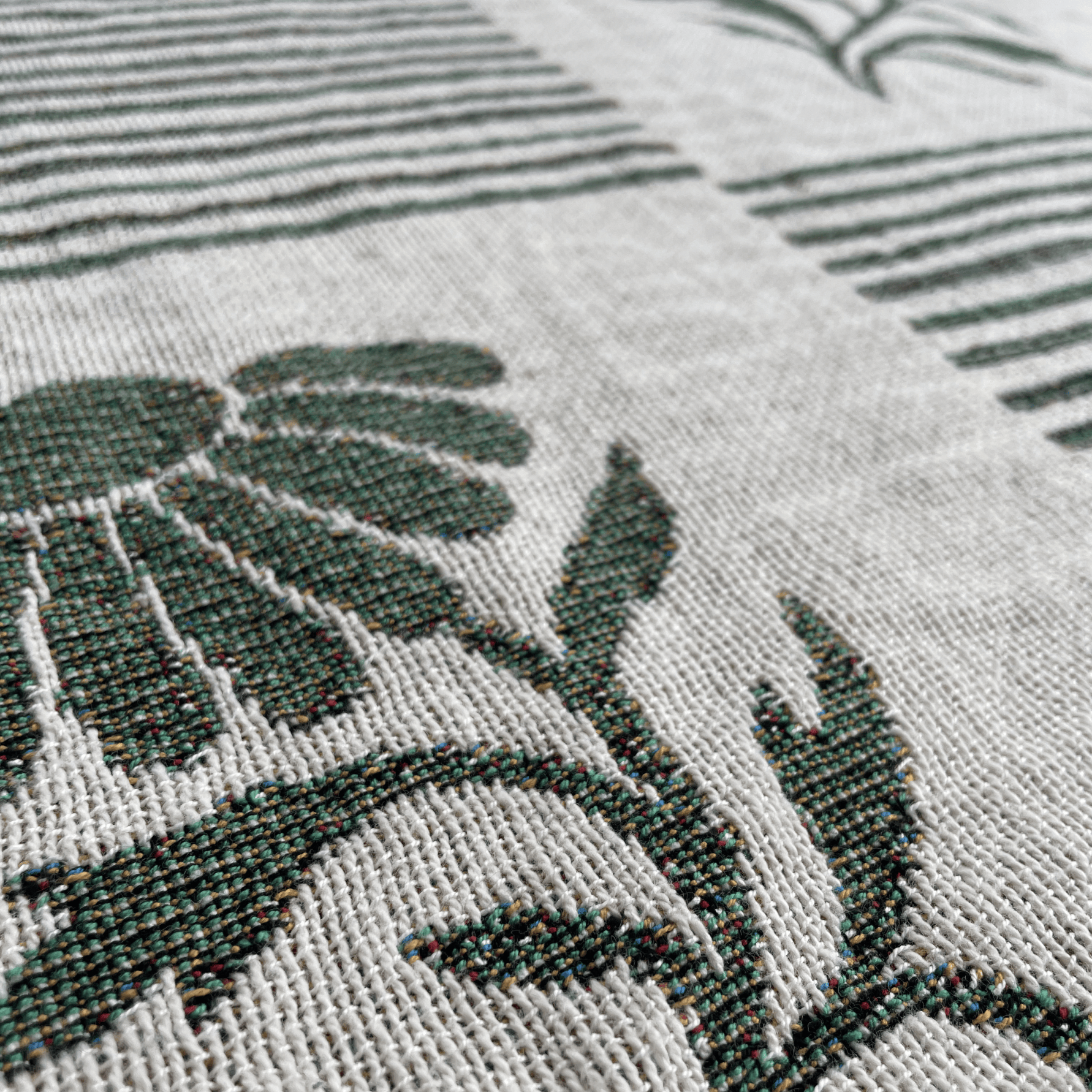Close-up of a woven textile with a dark green floral motif on a light beige background.
