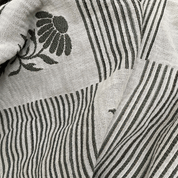 Close-up of a woven textile with vertical black stripes on an off-white base and a black floral motif in the upper left.