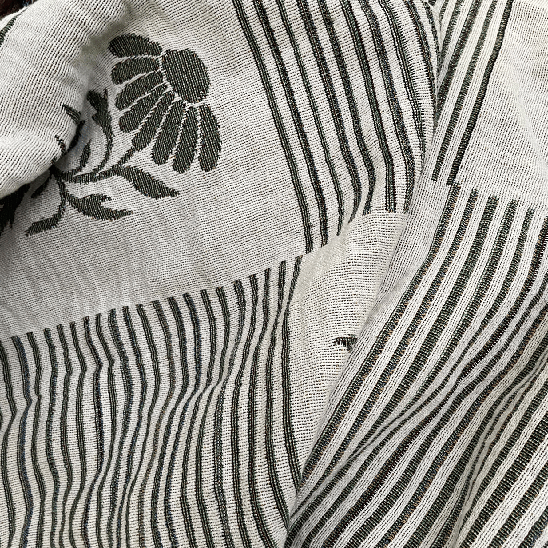 Close-up of a woven textile with vertical black stripes on an off-white base and a black floral motif in the upper left.