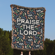Blanket with 'Praise the Lord' text and colorful patterns against a blue sky and green trees background