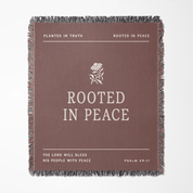 Brown blanket with 'Rooted in Peace' text and floral design on a white background