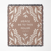 Blanket with leaf pattern and text 'Peace be to this house Luke 10:25' on a beige background