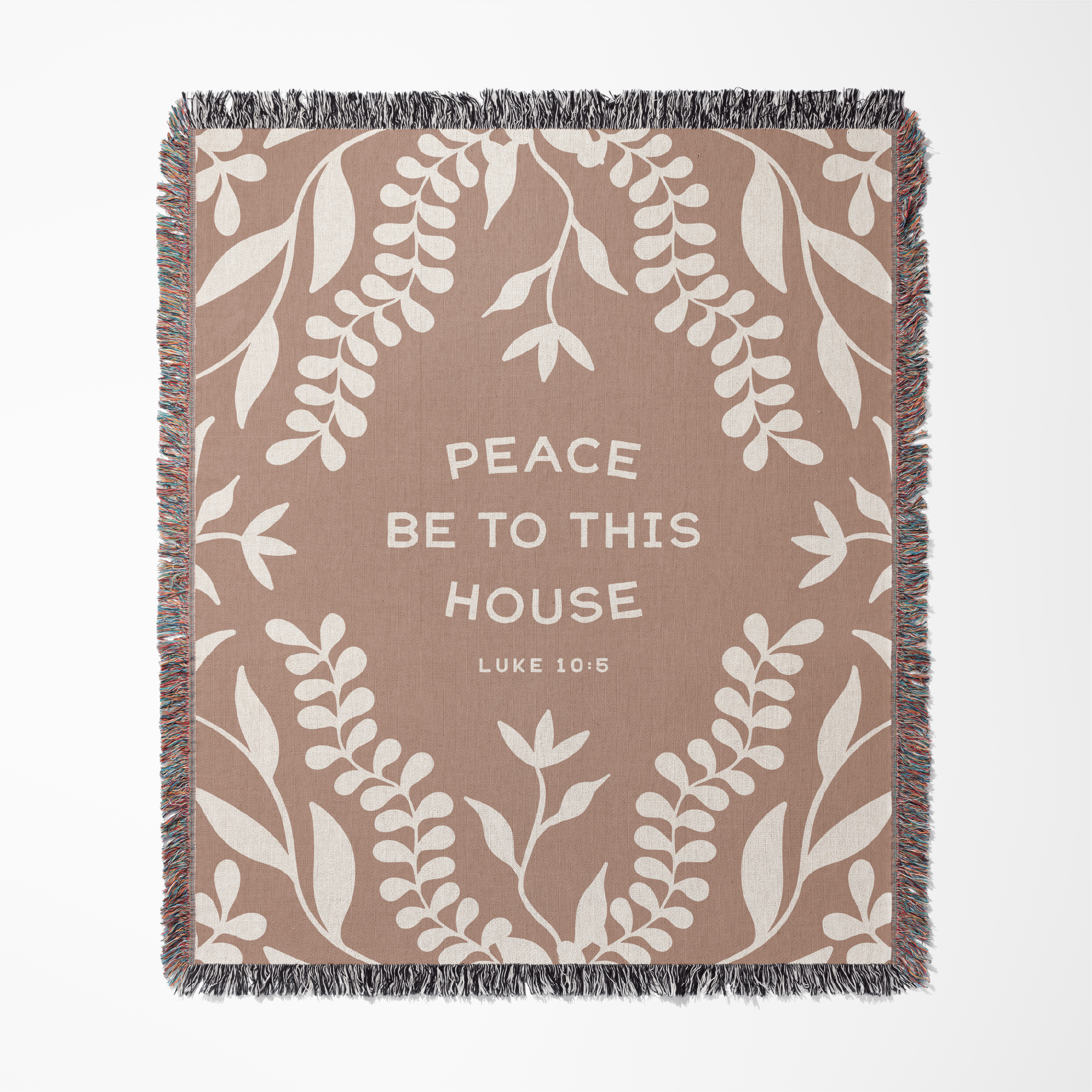 Blanket with leaf pattern and text 'Peace be to this house Luke 10:25' on a beige background