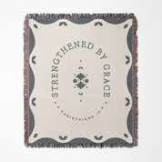 Blanket with 'Strengthened by Grace' text and decorative border on a white background