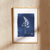 Framed artwork with blue ink wash and white botanical illustration on a beige wall.