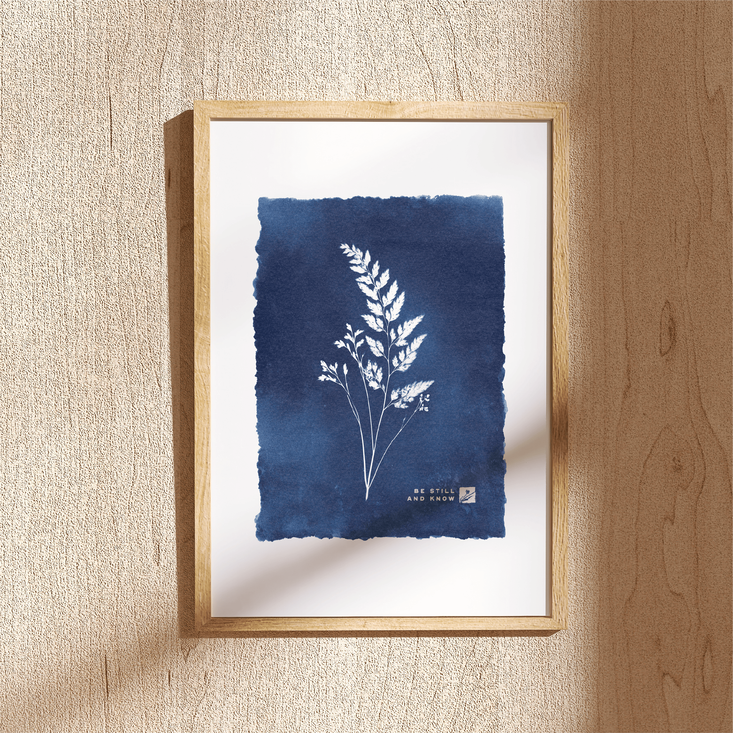 Framed artwork with blue ink wash and white botanical illustration on a beige wall.