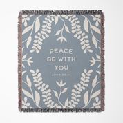 Woven blanket with leaf pattern and 'Peace be with you' text on a blue background