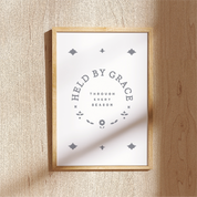 Framed print with 'Held by Grace' text on a wooden wall.