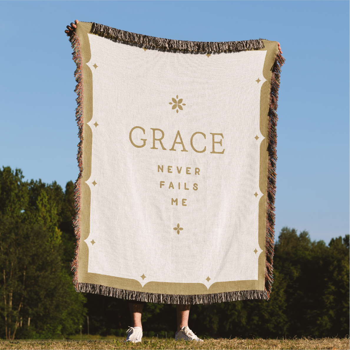 Blanket with 'GRACE NEVER FAILS ME' text in a natural setting
