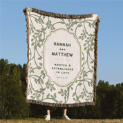 Blanket with 'Hannah and Matthew' text and foliage design, held by a person outdoors.