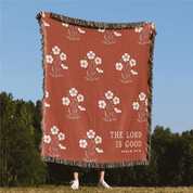 Blanket with floral pattern and 'The Lord is Good' text in a natural setting