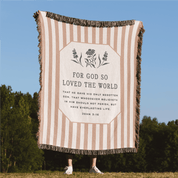 Striped blanket with text and design on a grassy field with trees in the background