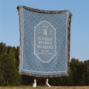 Decorative throw blanket with text and patterns on a grassy field with trees in the background