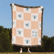 Checkered blanket with bee patterns and 'Kind Words Are Like Honey' text, held by a person outdoors.