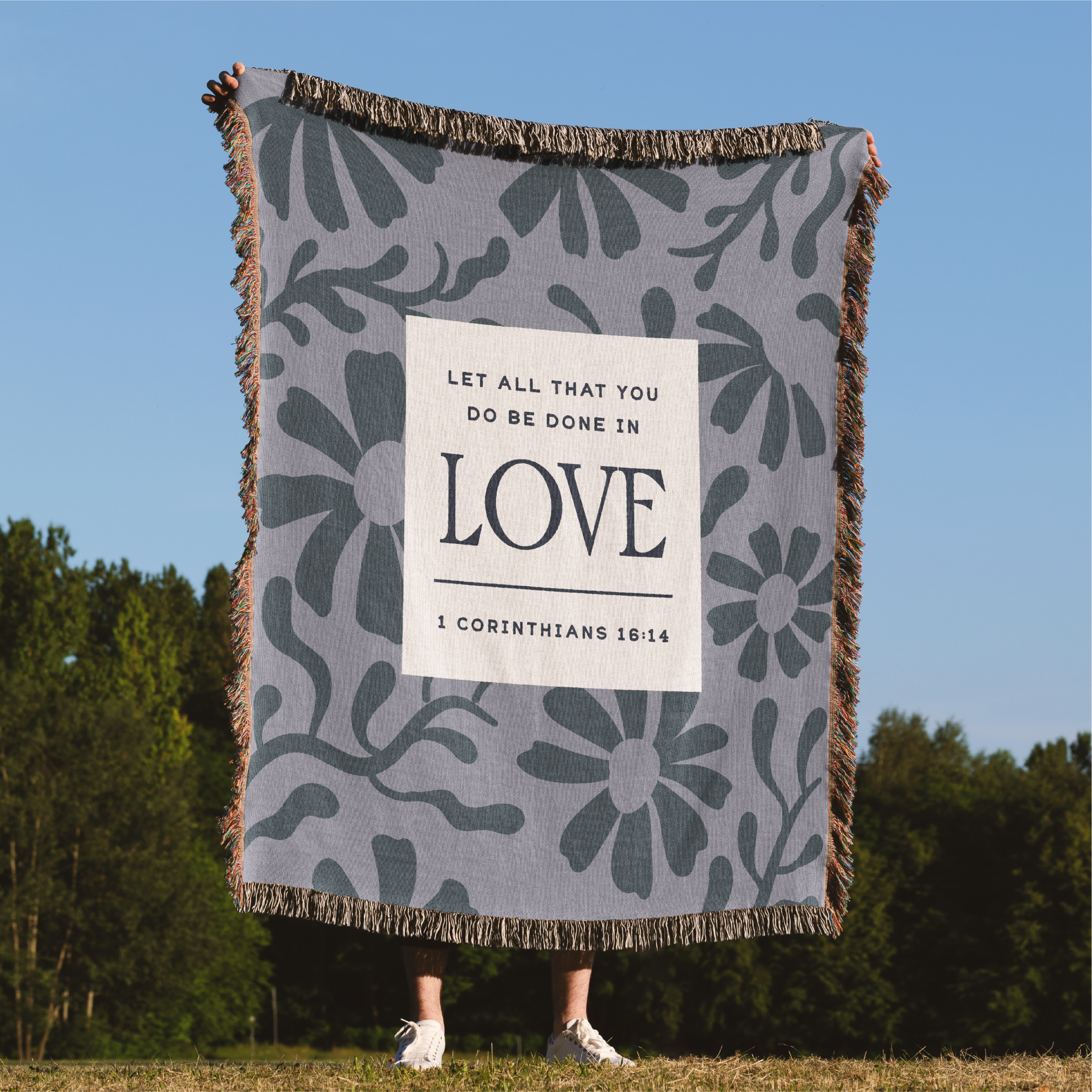 Person holding a floral-patterned blanket with a motivational quote against a natural background