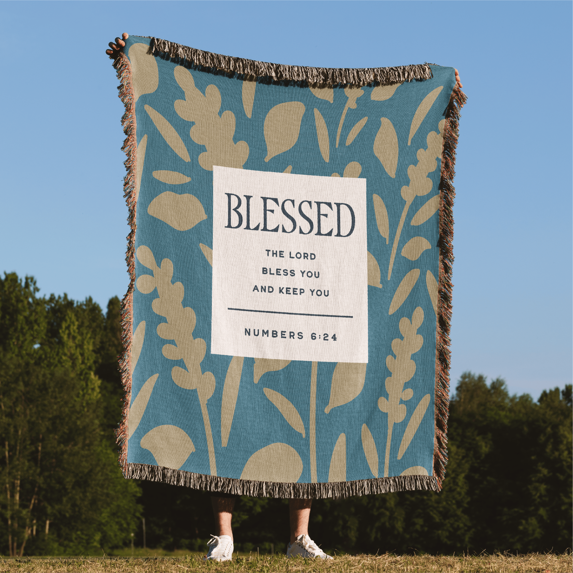 Blanket with 'Blessed' text and plant design in a natural setting