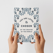 Notebook with 'You are loved & chosen' text held by hands on a light gray background