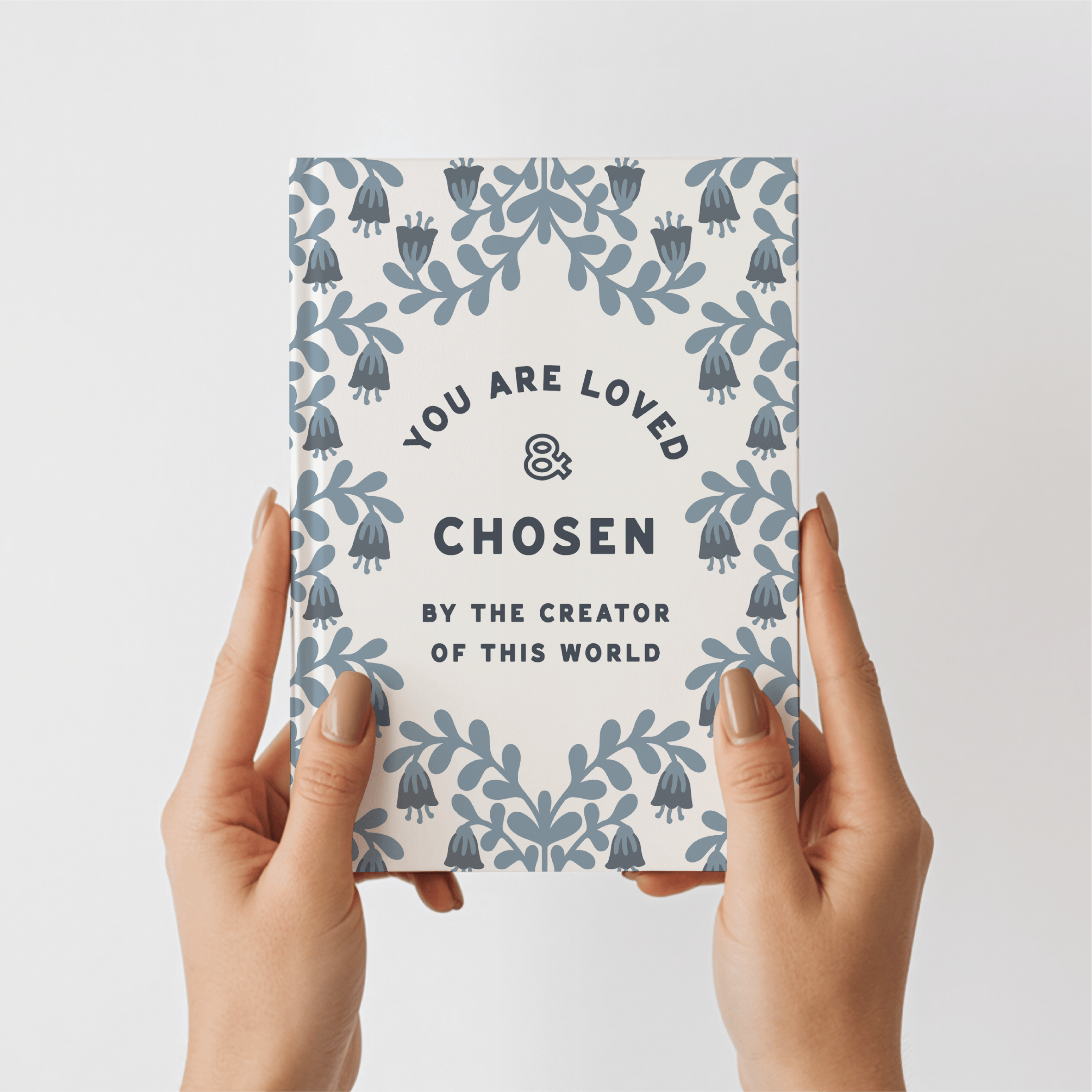 Notebook with 'You are loved & chosen' text held by hands on a light gray background