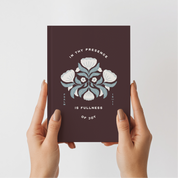 Hands holding a dark brown book with floral design and text on a light gray background