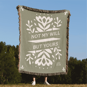 Green blanket with white text and floral patterns, held by a person outdoors.