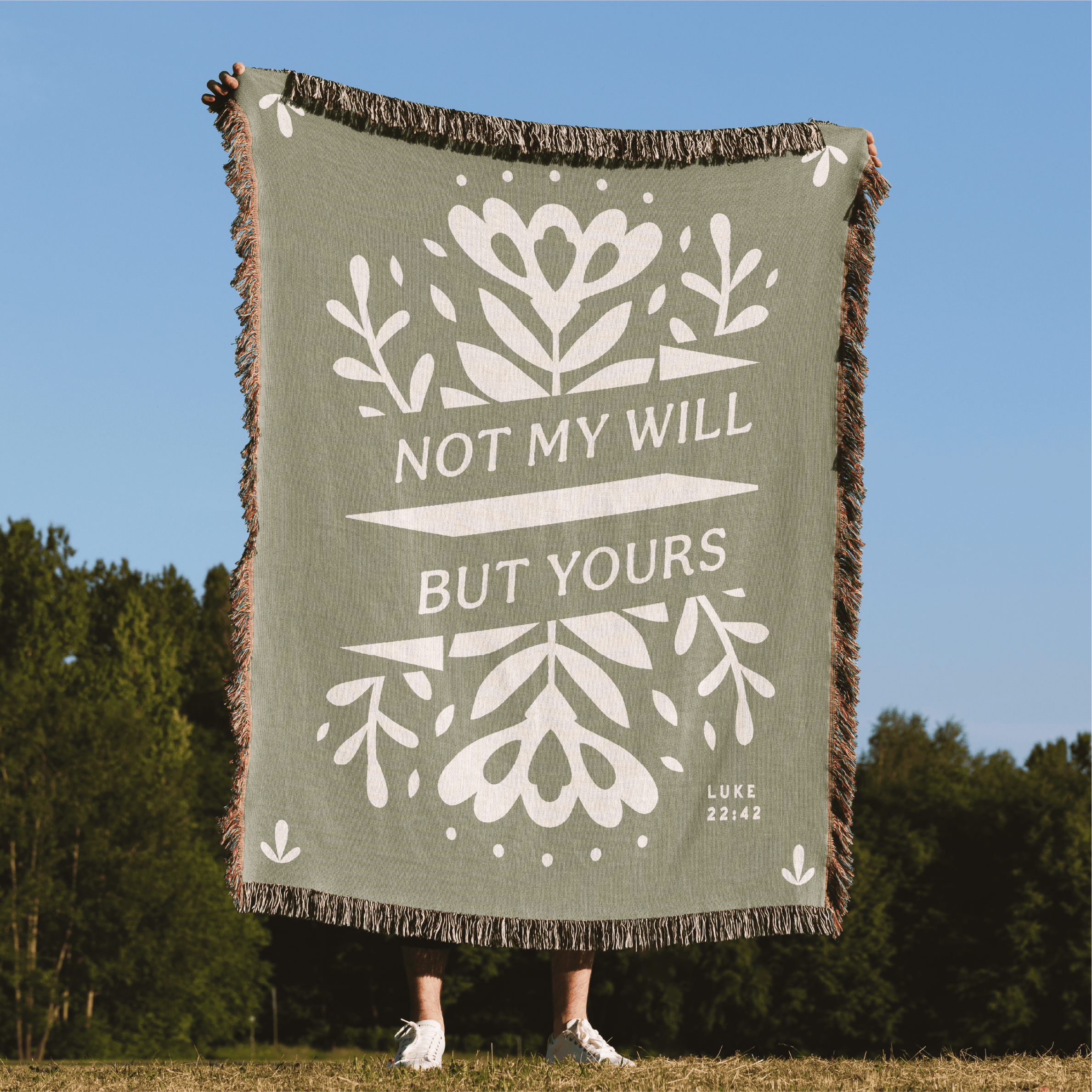 Green blanket with white text and floral patterns, held by a person outdoors.