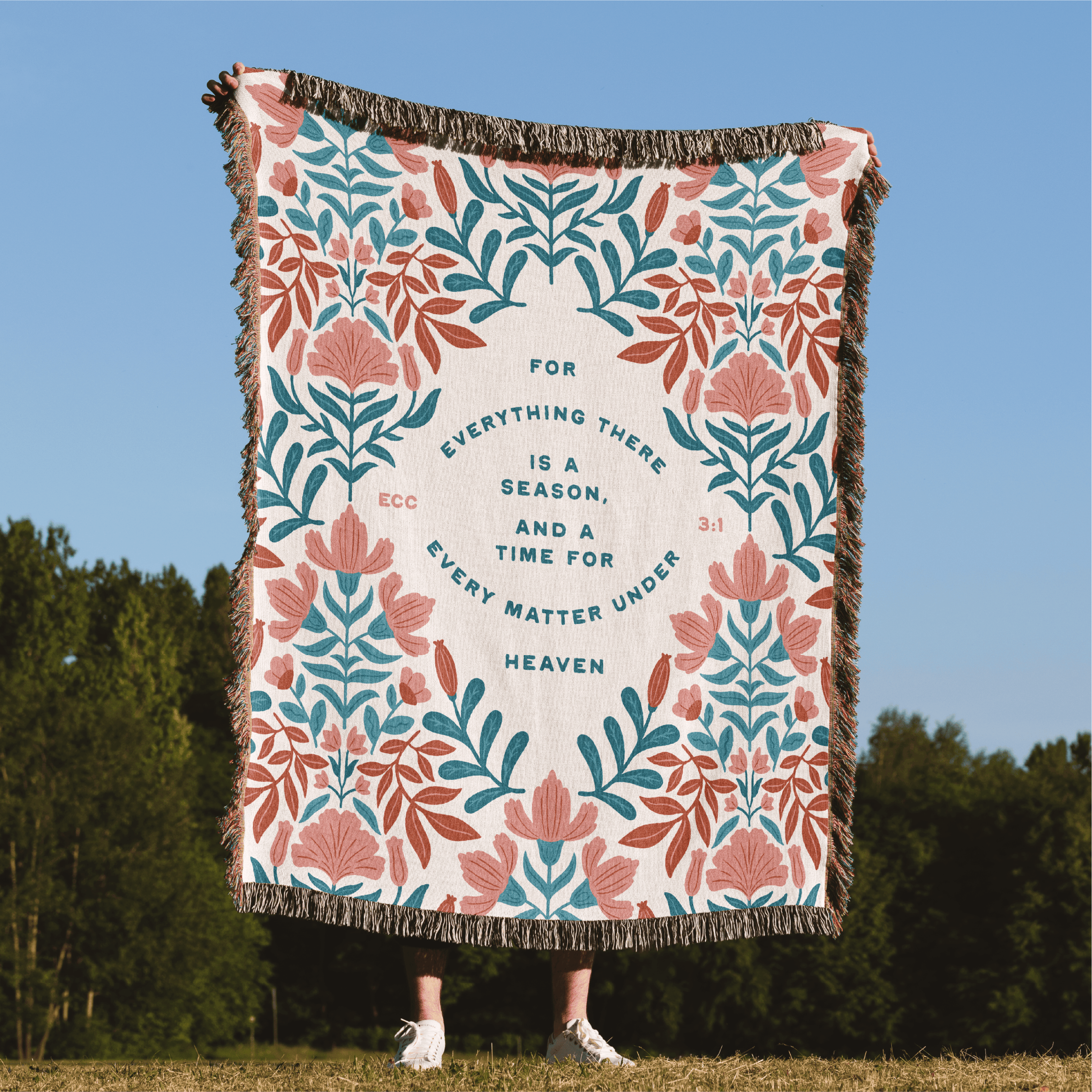 Floral patterned throw blanket with text on a grassy field with trees in the background