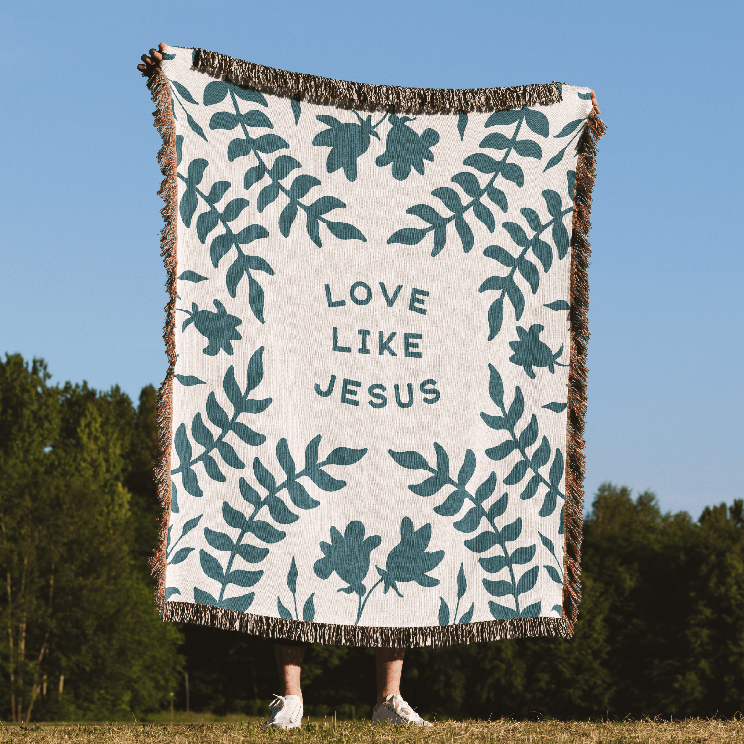 Blanket with leaf pattern and 'Love Like Jesus' text in a natural setting