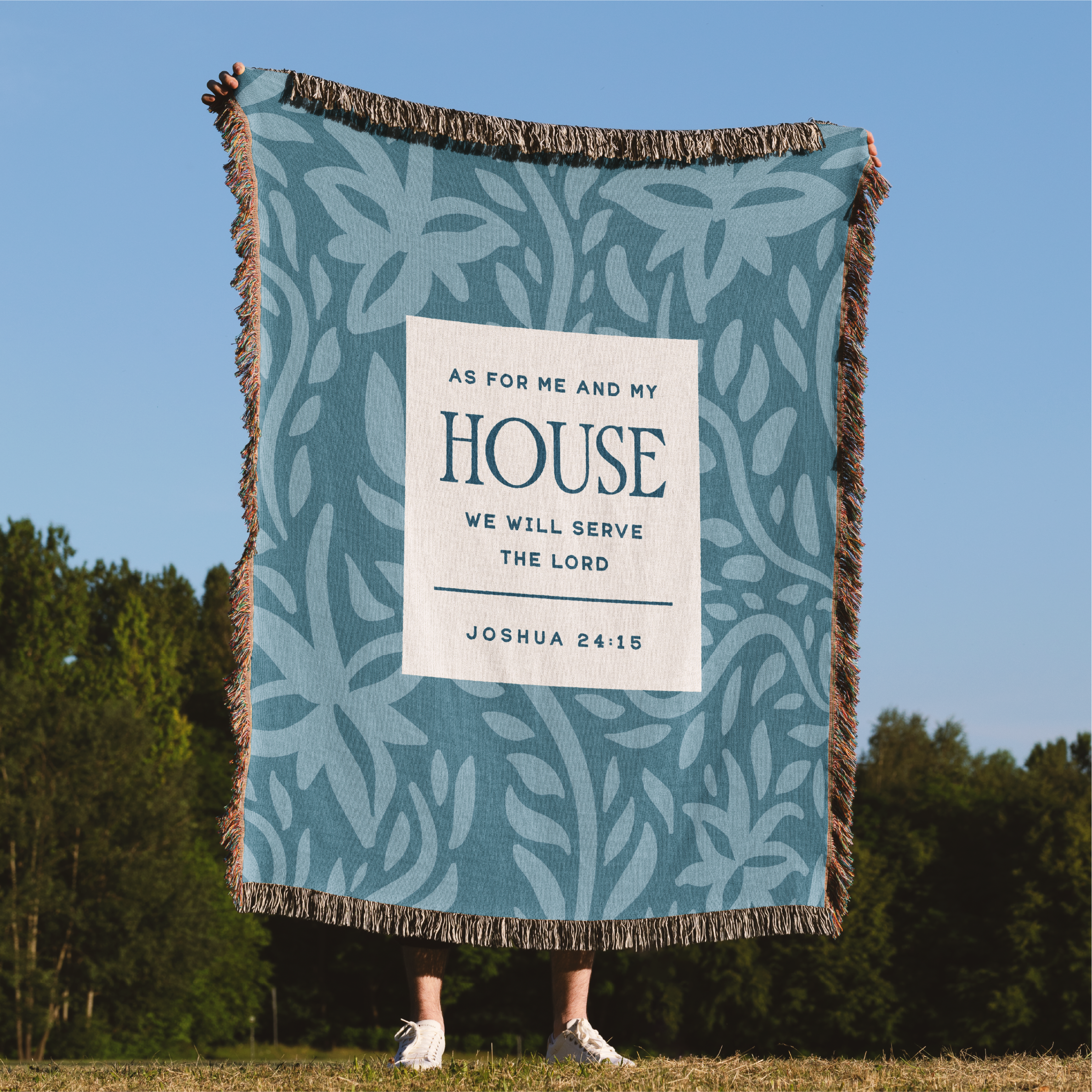 Person holding a decorative blanket with a biblical quote against a natural background