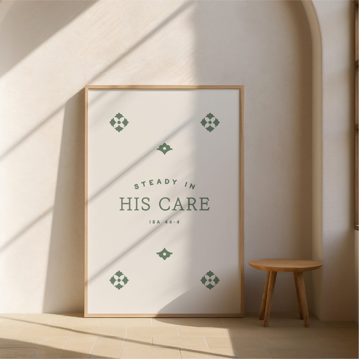 Framed poster with 'Steady in His Care' text in a minimalistic room with a wooden stool.