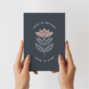 Dark blue notebook with floral design and text held by hands on a light gray background