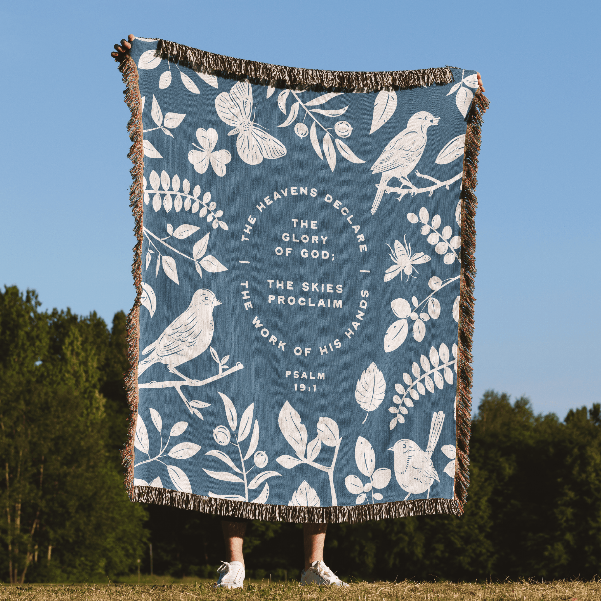 Blanket with nature-themed design and Psalm 19:1 text, displayed outdoors.