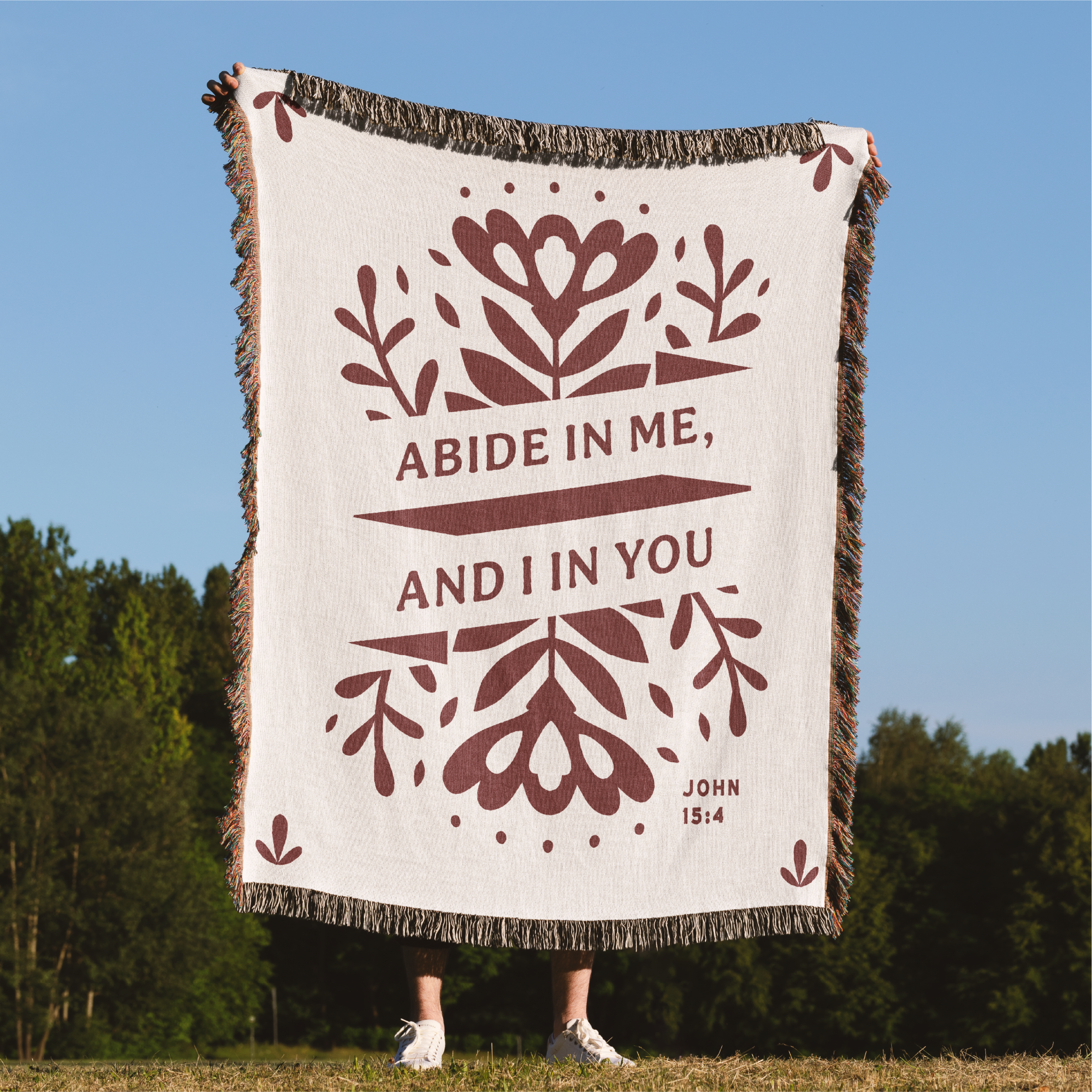 Blanket with 'Abide in me, and I in you' text and floral designs outdoors