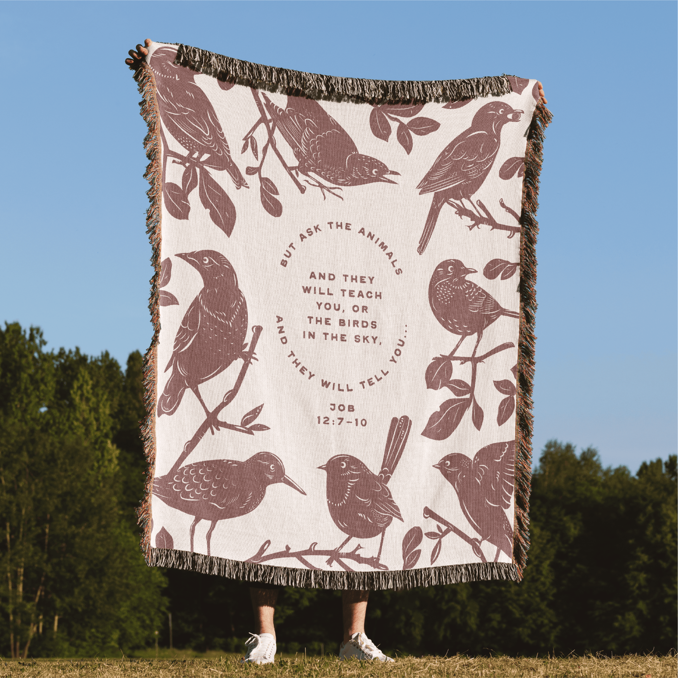 Blanket with bird design and text on a grassy field with trees in the background