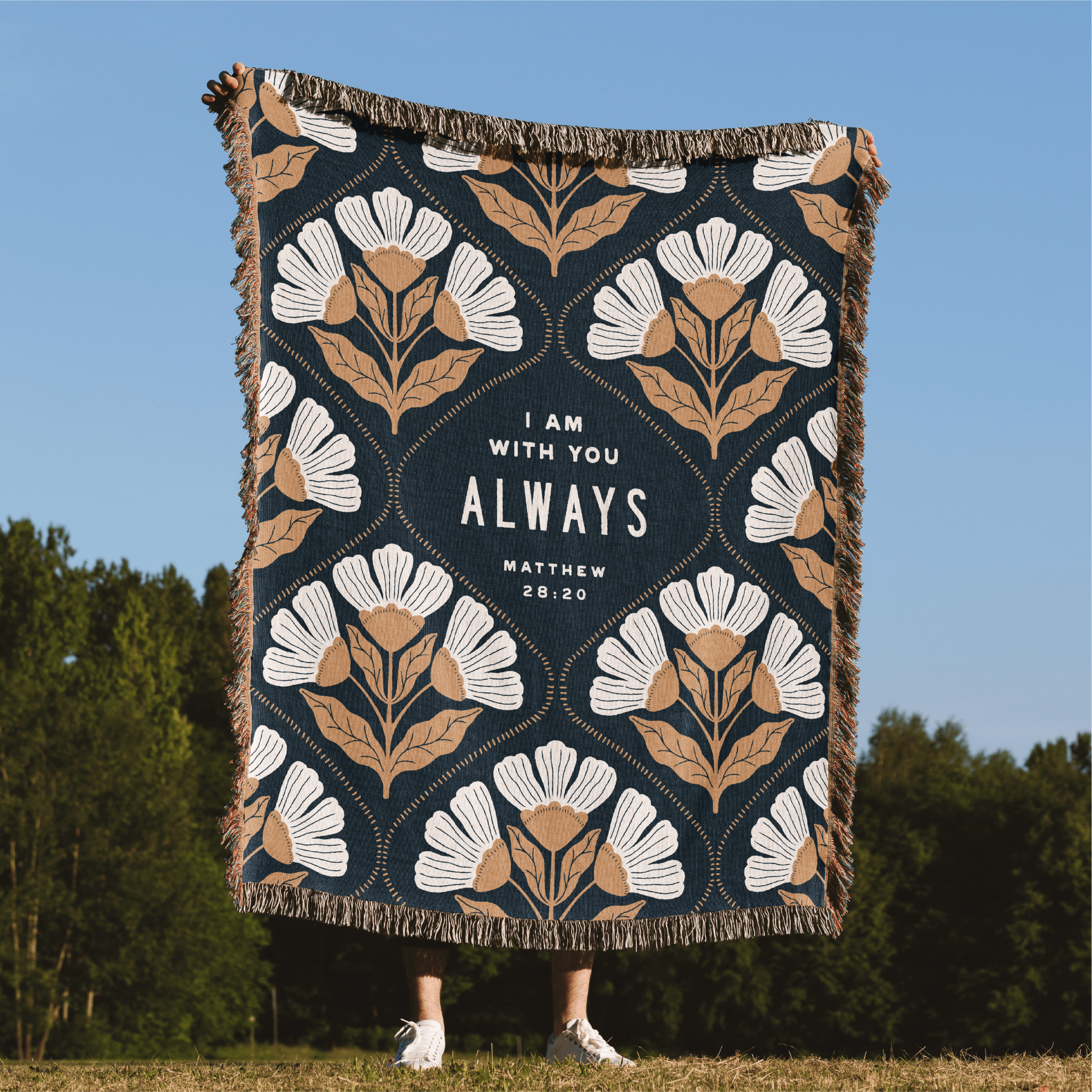 Floral patterned blanket with 'I am with you always' text against a blue sky and green trees background