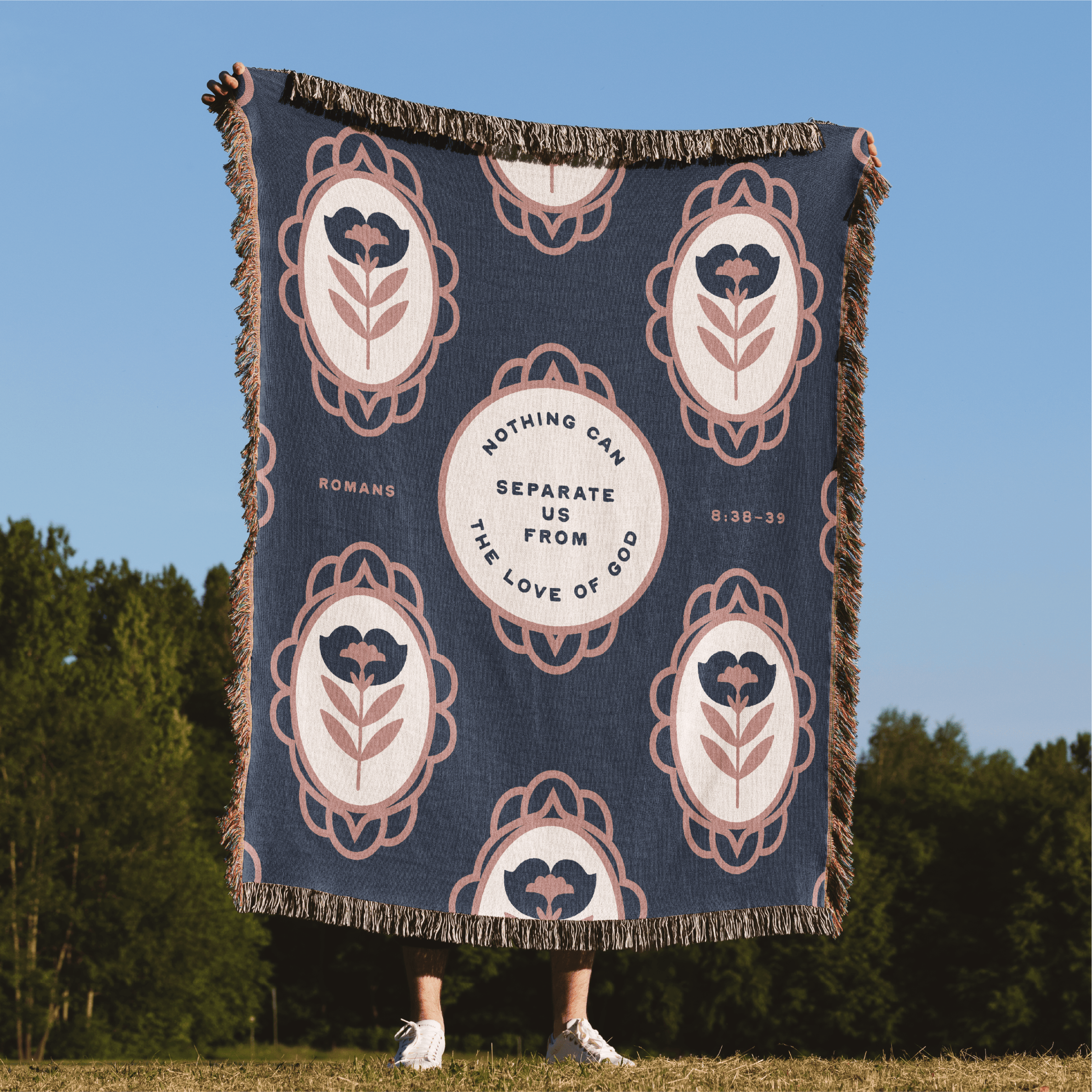 Decorative blanket with motivational quote and floral patterns on a grassy field with trees in the background