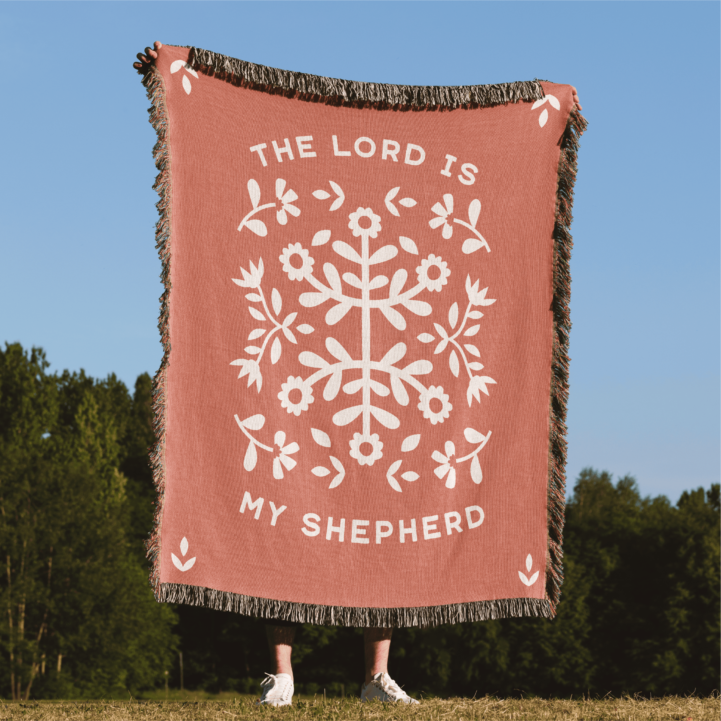 Blanket with floral design and 'The Lord is my Shepherd' text in a natural setting