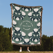 Decorative blanket with floral pattern and text, displayed outdoors against a blue sky and trees.