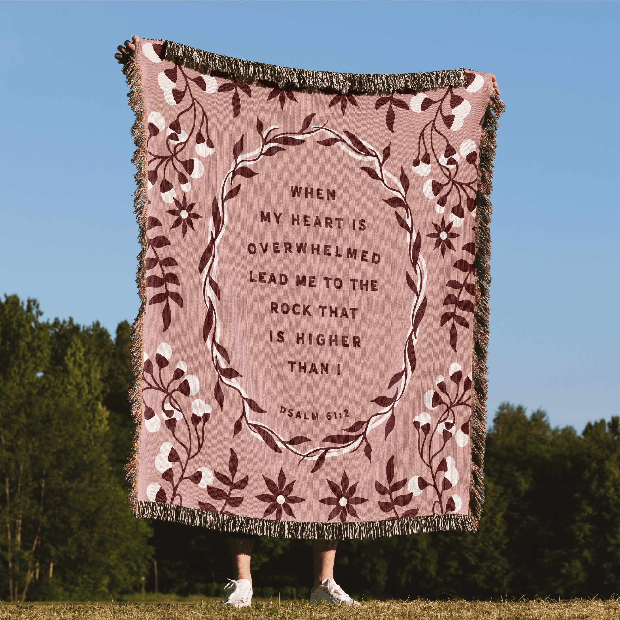 Pink blanket with floral design and text against a blue sky and green trees background